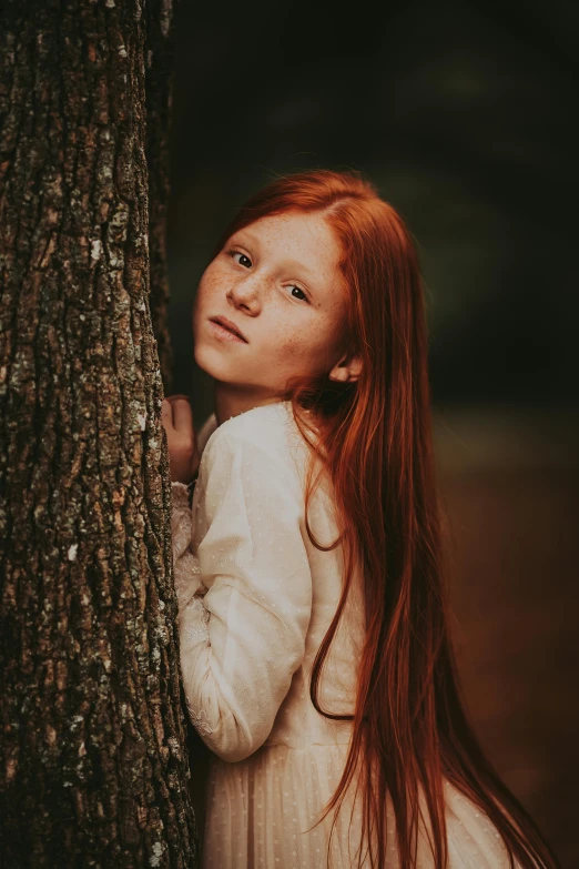 a red headed girl leans against a tree and poses