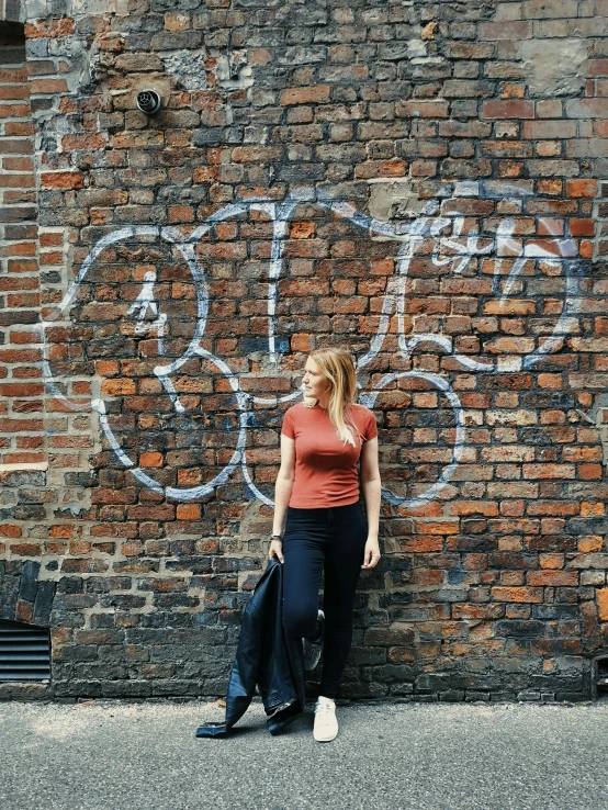 a girl standing on a sidewalk by a brick wall