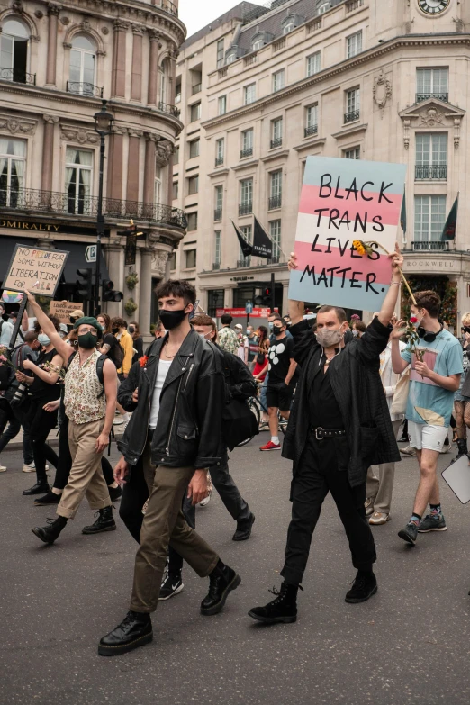 people walk in the street with black trans lives matter sign