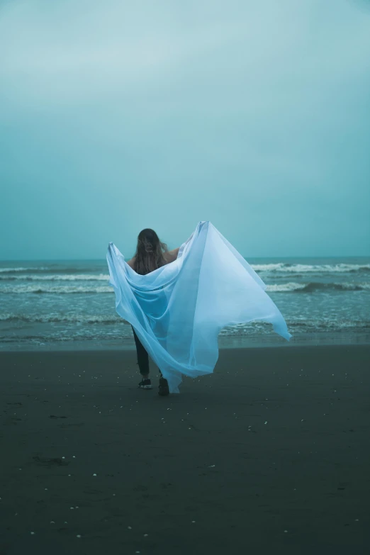 a woman walks along the beach, covering her face with a scarf