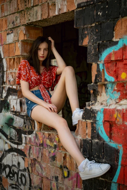 a young lady with white shoes posing for the camera on a brick wall with graffiti