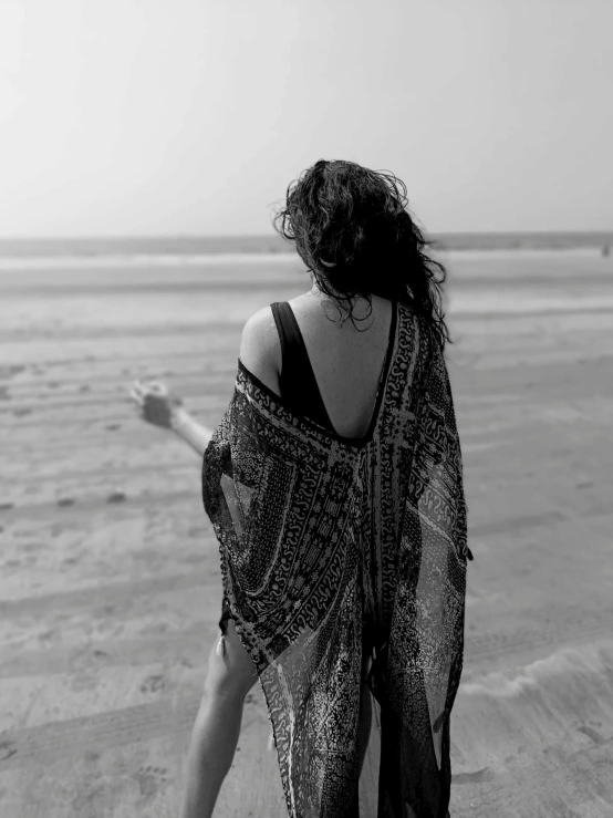 a woman in an open sarong on the beach looking into the ocean