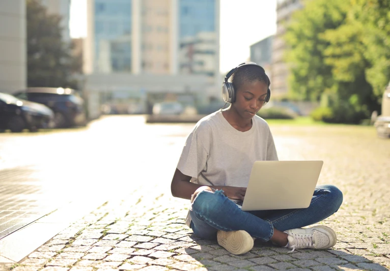 a woman is sitting on the street using her laptop