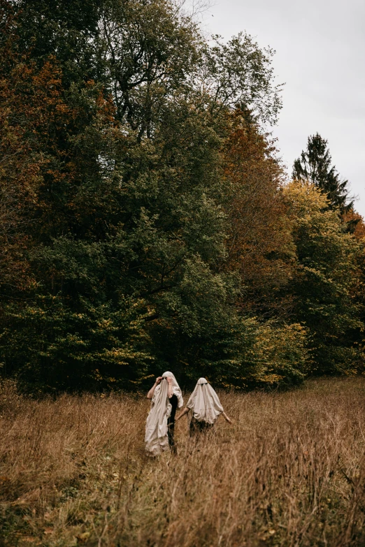 two people in white cloaks walk through tall grass