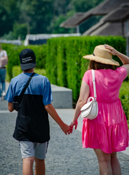 two people walking down a path in front of green hedges