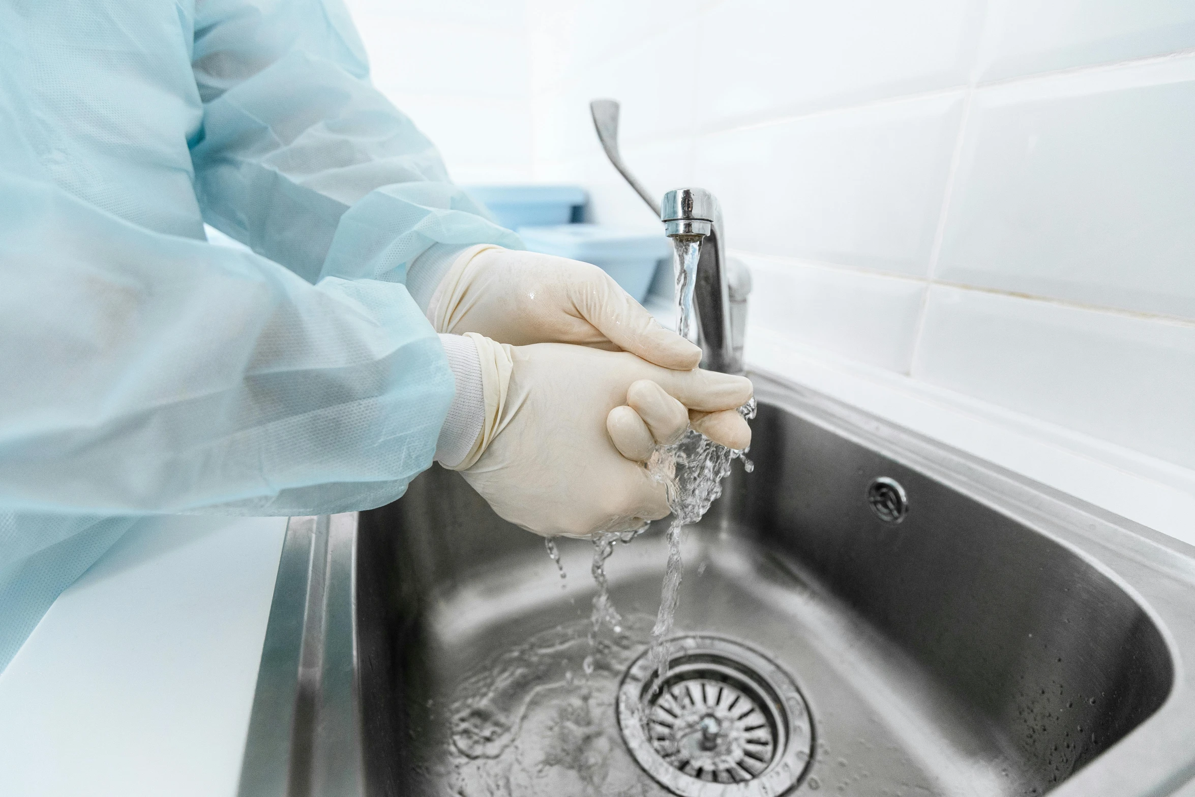 a person in white gloves, in gloves and rubber gloves washes his hand in a kitchen sink