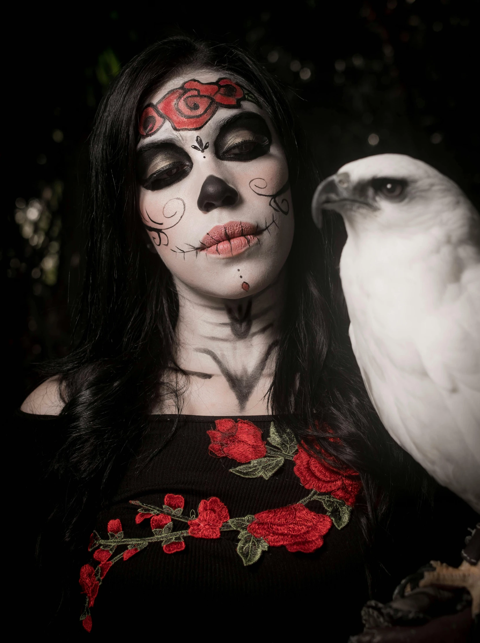 a woman with painted faces and white feathers is next to a white parrot