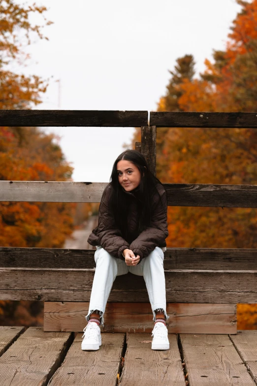 a woman is sitting on a wooden deck in autumn