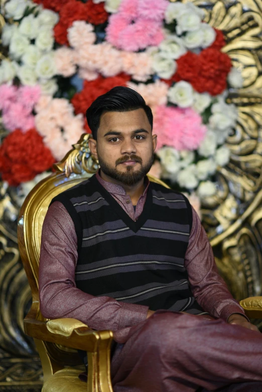 a man sitting in a chair with a flower display behind him