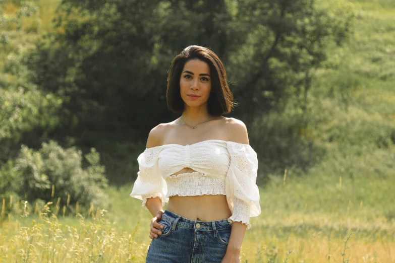 a woman standing in a field of grass wearing an off the shoulder crop top