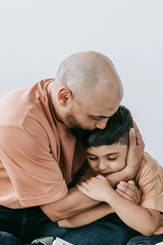 the man is hugging the little boy's face while he sits