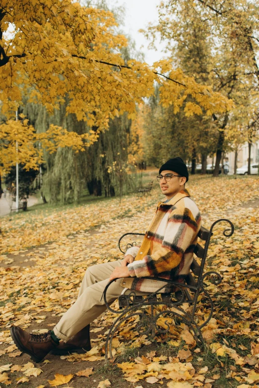 a man is sitting on a park bench surrounded by leaves