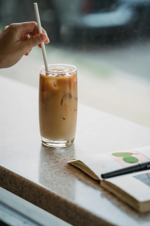 person holding a straw in a drink next to a book