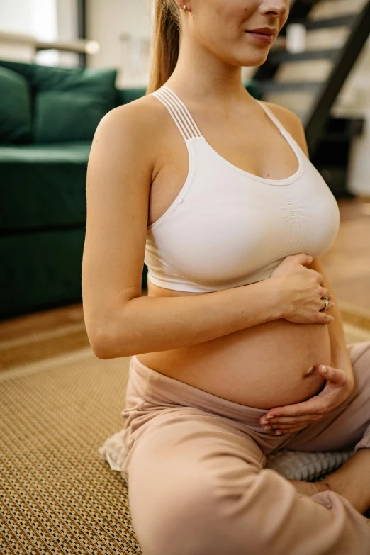 a pregnant woman sitting on the floor wearing yoga pants