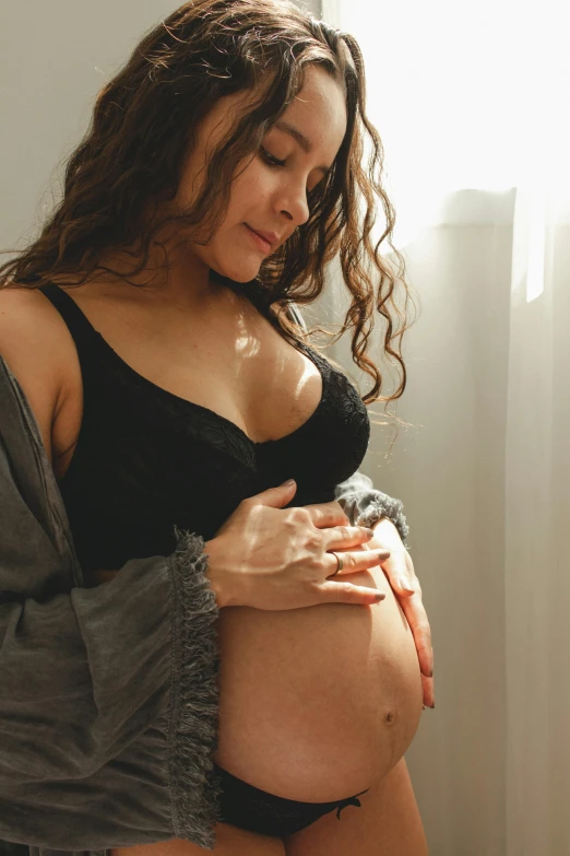 pregnant woman sitting on bed holding onto her stomach