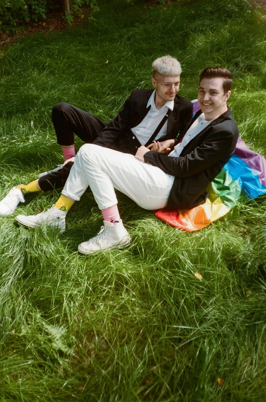 two men wearing suits sitting on a blanket in the grass