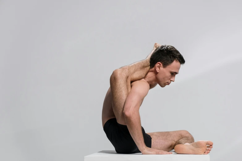 a shirtless man sits on a ledge while stretching