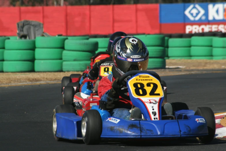 three people driving cars on a track with spectators behind them