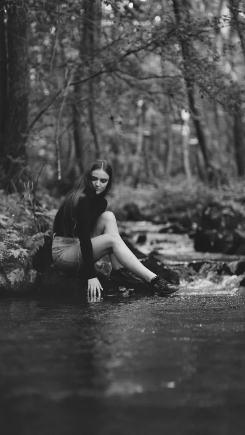 woman sitting on rock in creek with trees in background