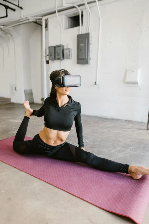 a young woman wearing a virtual - based device sits on a yoga mat and looks at the viewer