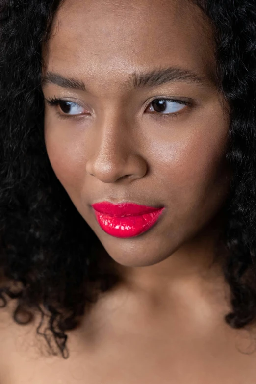 a closeup s of a young woman with curly hair, wearing a red lip paint