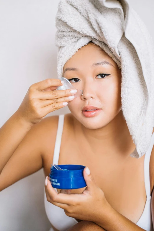 a woman with a towel wrapped around her head uses a face cream