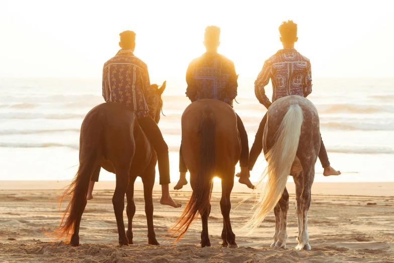 three men wearing period costumes riding horses on the beach