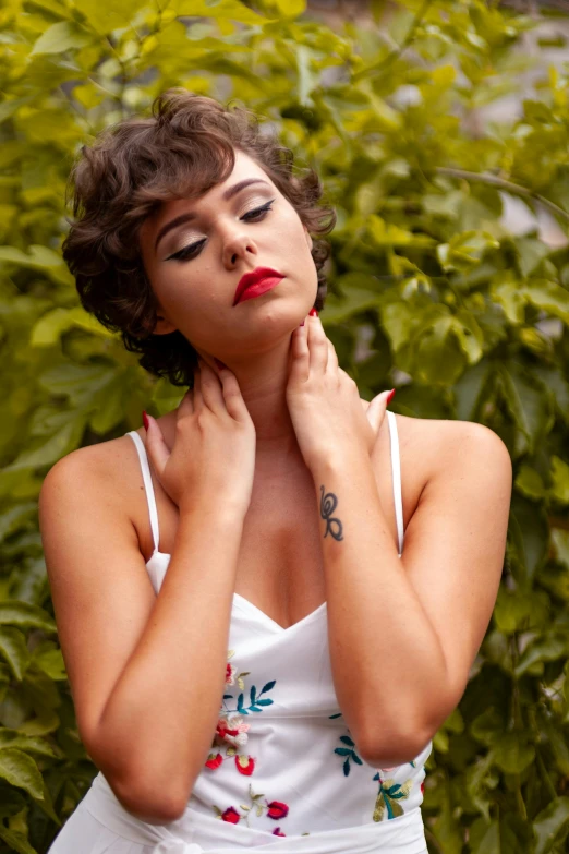 a woman standing by bushes looking up with her hands on her chest