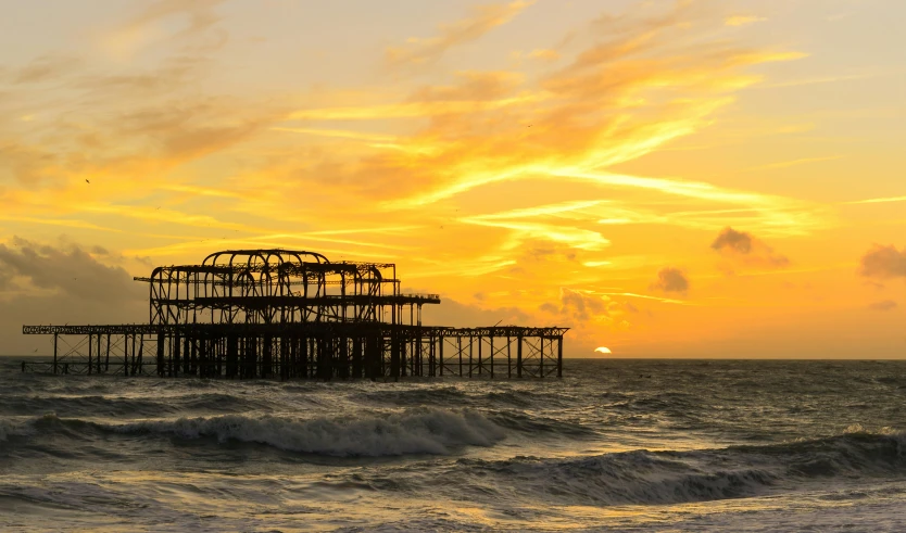 the sun sets on a beach with old fishing platforms