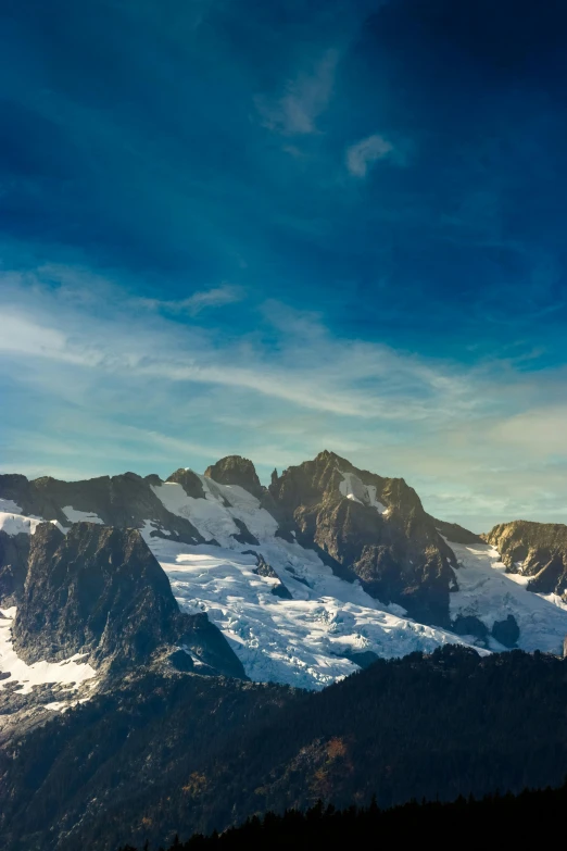 a scenic view of snow - covered mountains under a cloudy blue sky