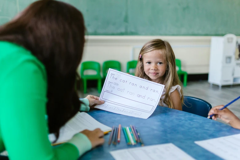 a girl with pencils smiling while another child holds up a paper