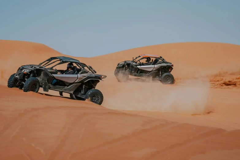 a couple of cars driving through sand dunes