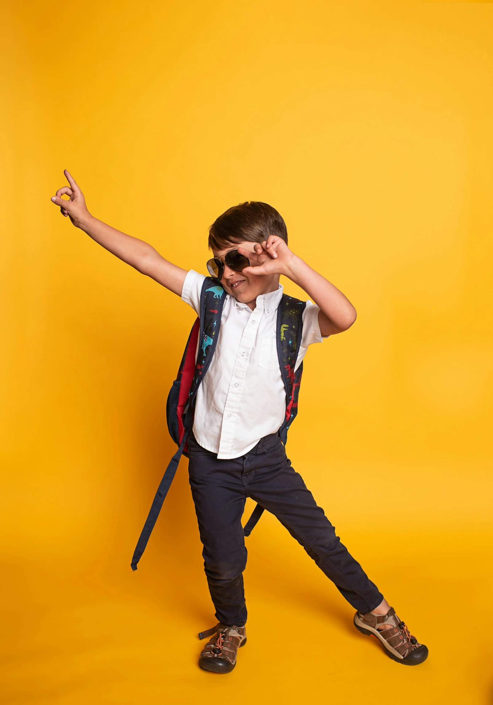 a boy wearing a backpack and glasses, holding a pair of jeans and pointing up