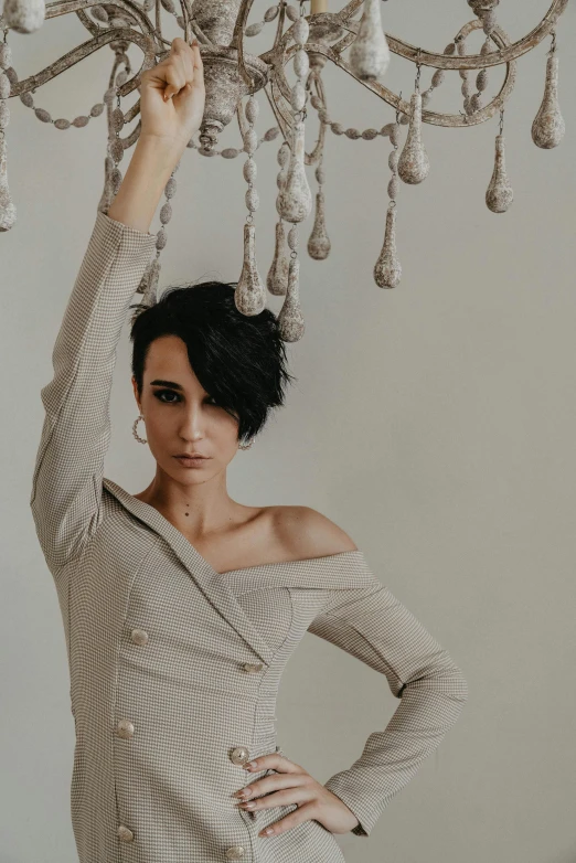 a woman wearing an off the shoulder top with her hands on a chandelier