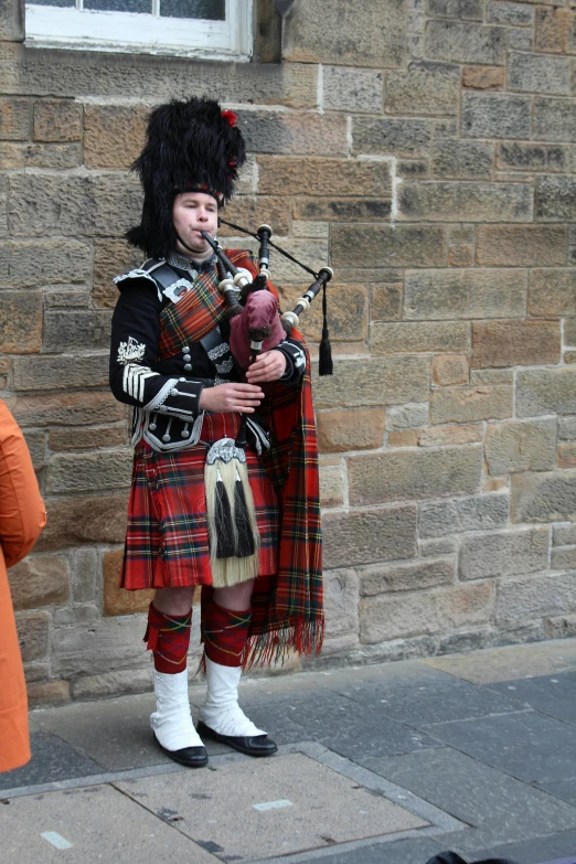a person playing bagpipes on the street near a brick building