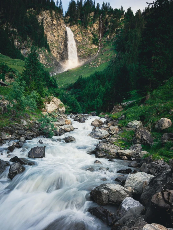 the waterfall is going down the mountain with rocks on the bank