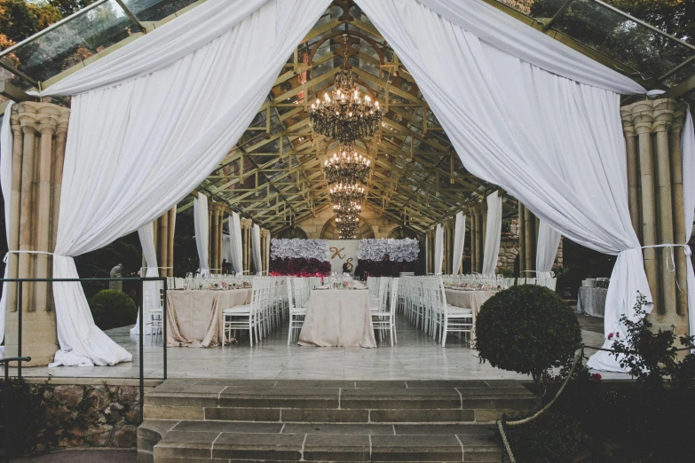 wedding reception tables are under white curtains with draps