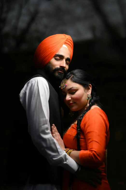 a man and woman hugging each other while wearing orange turbans