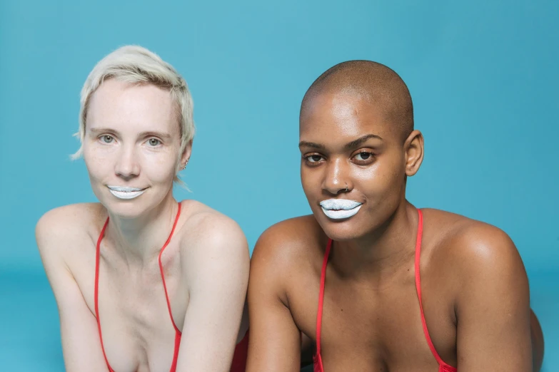 two women with white teeth and hair sitting on a blue background