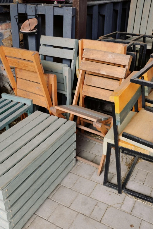 a group of wood chairs are outside by some trash