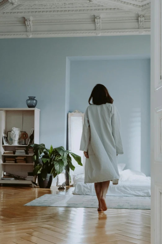 woman walking into a room that contains a bed, a window and hardwood floor