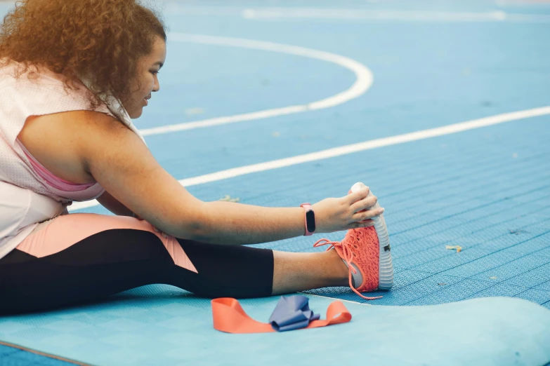 a woman sits on a blue surface, tying her shoelace