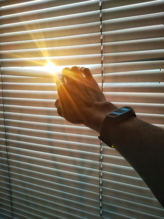 a hand holding onto a blind with sun light coming through