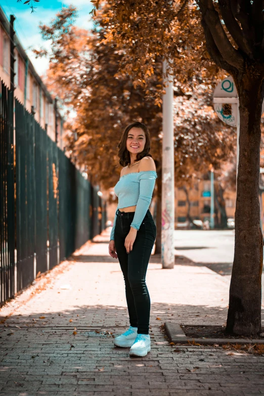 an asian girl posing in front of a tree on the sidewalk