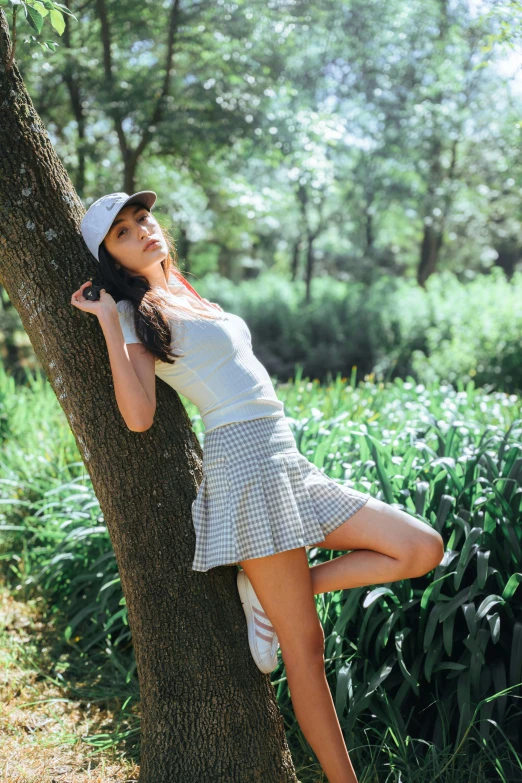 young woman in a short dress leaning up against a tree in a forest