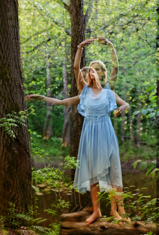 a girl in a blue dress is standing by some trees