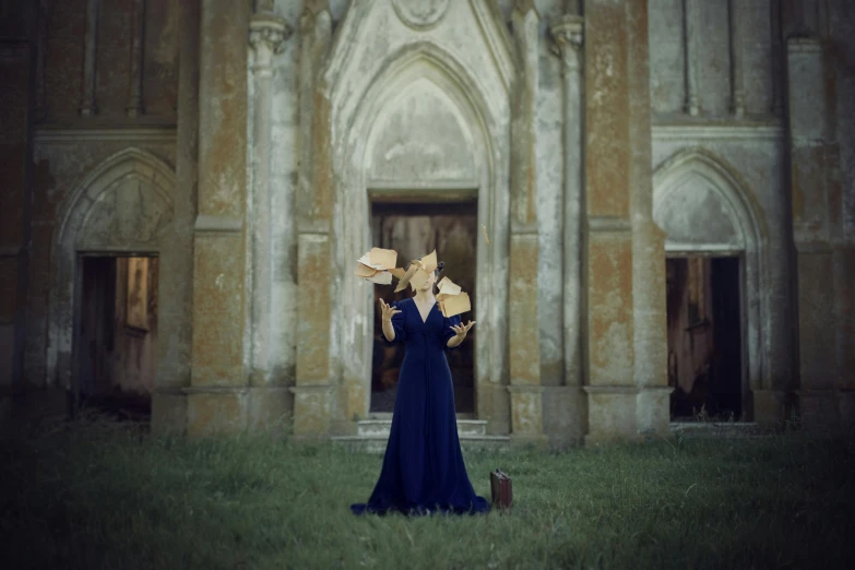 a woman wearing a long blue dress stands holding some gold flowers