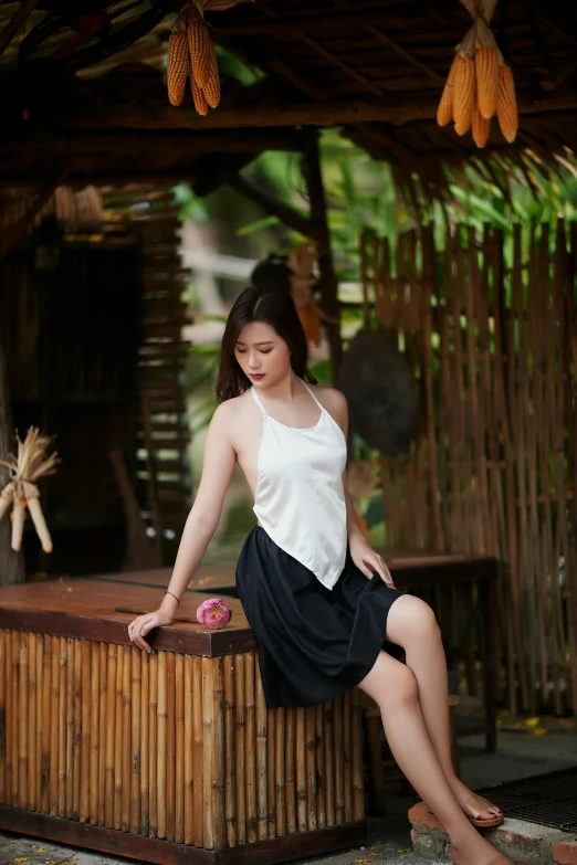 an asian woman poses sitting on a bamboo bench