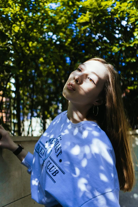 a woman in blue shirt looking up at a tree