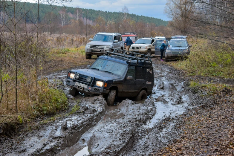 several cars traveling down a muddy road with one offroad